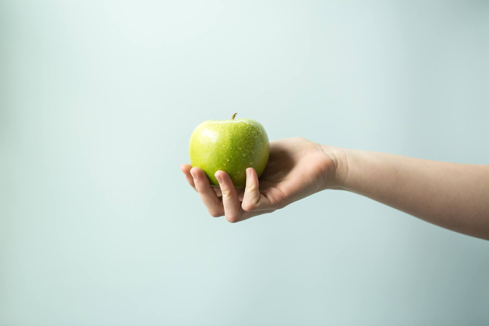 A woman's hand clutching a vibrant green apple.