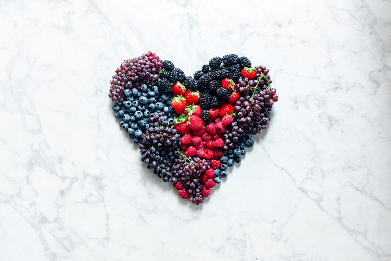 A antioxidant-rich heart-shaped arrangement of berries displayed on a smooth marble surface.