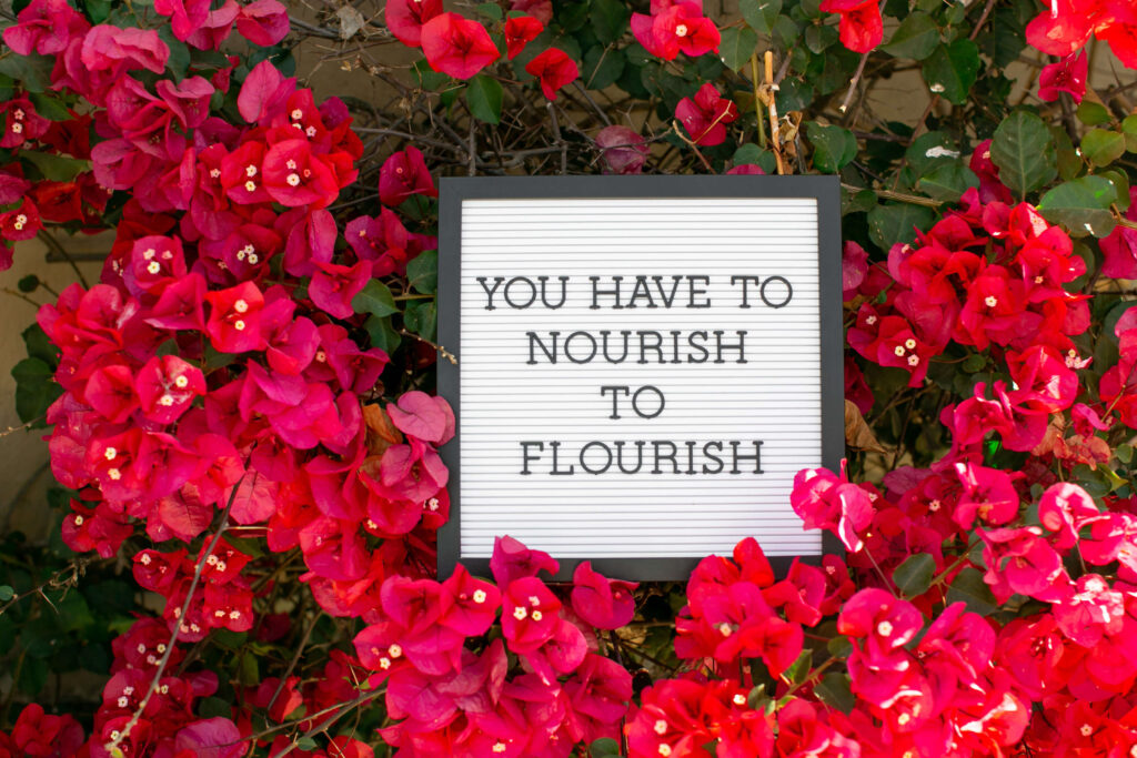 You have to nourish to flourish sign in a bed of flowers