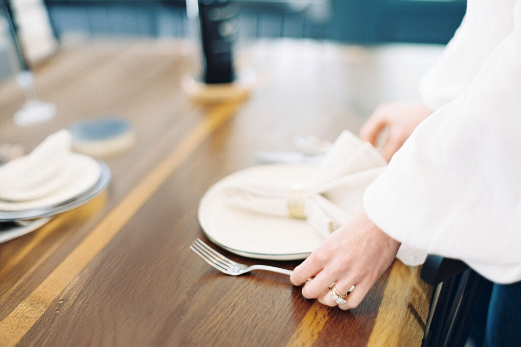 A person embraces a non-diet approach while setting a wooden table, placing a white napkin and silver fork neatly beside a plate.